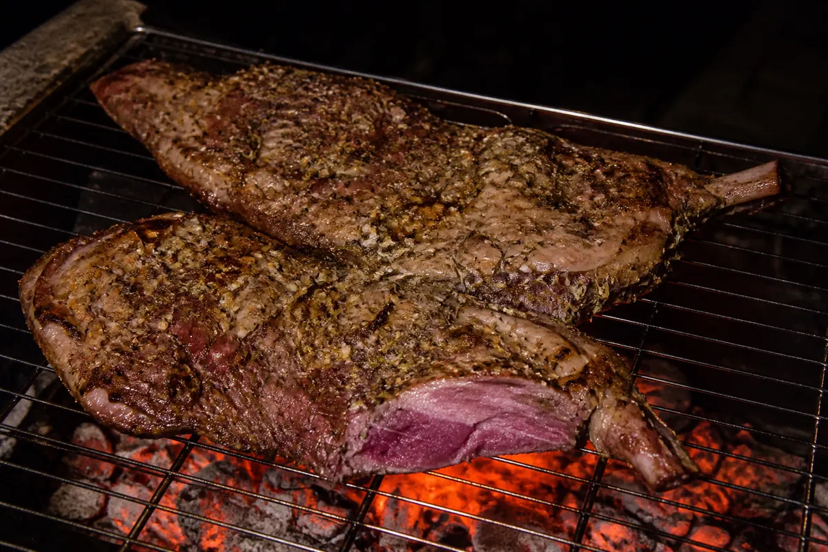 A butterflied leg of lamb, flat on the grid